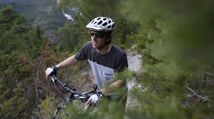 Ein Mountainbiker schiebt sein Rad auf einem Trail in den Bergen. | © DAV/Wolfgang Ehn